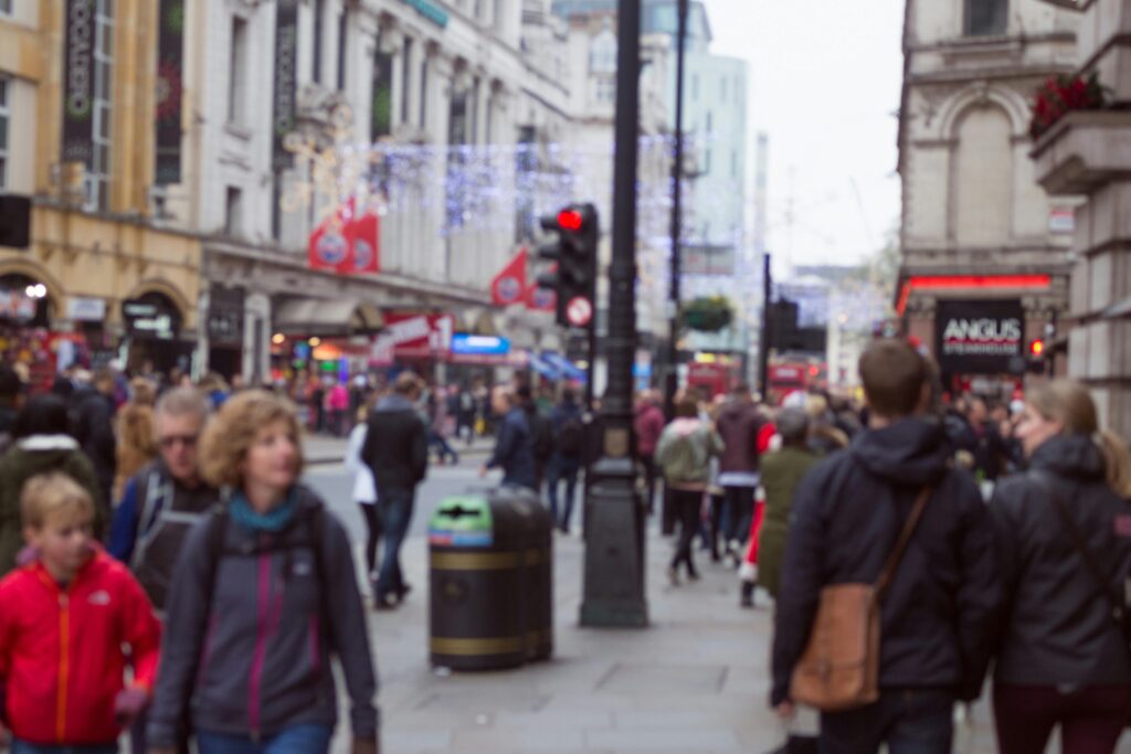 Busy urban street scene with crowds walking past decorated shops.